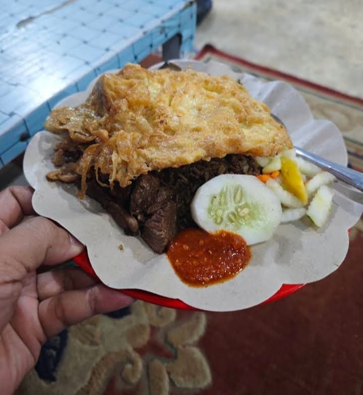Fried rice with omelet, beef, cucumber, pickles, and chili sauce on a red plate.